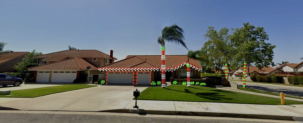 Festively lit house with palm trees and trucks, showcasing vibrant holiday decorations at night.