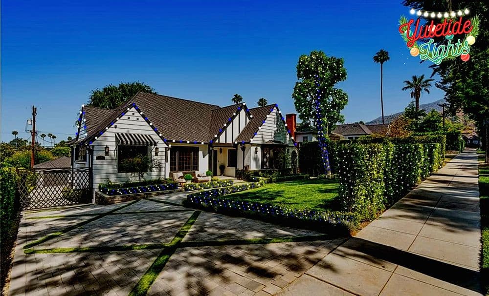 Charming house decorated with festive lights, surrounded by manicured lawns and palm trees.