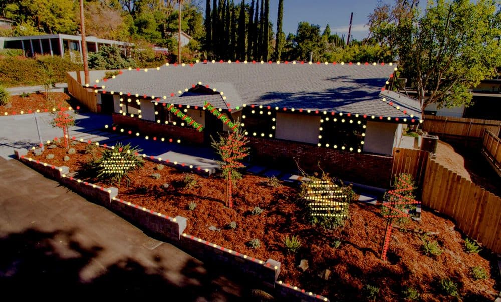 Decorated house with colorful Christmas lights and festive landscaping in a suburban neighborhood.