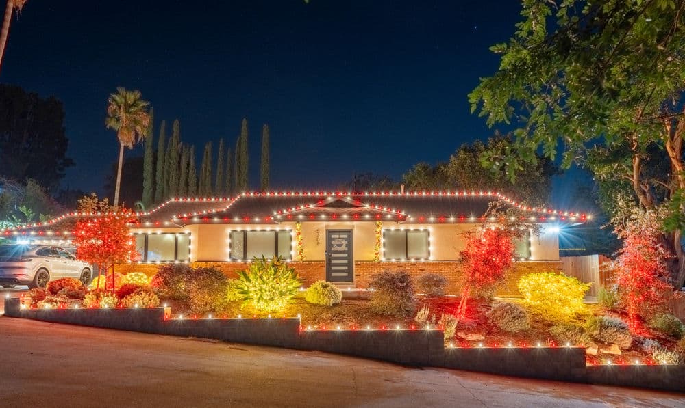 Festively lit house at night with colorful lights and vibrant landscaping.