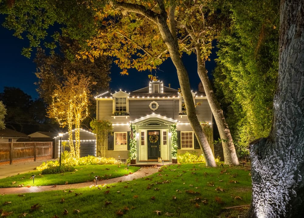 Charming house adorned with twinkling lights, surrounded by lush greenery at night.