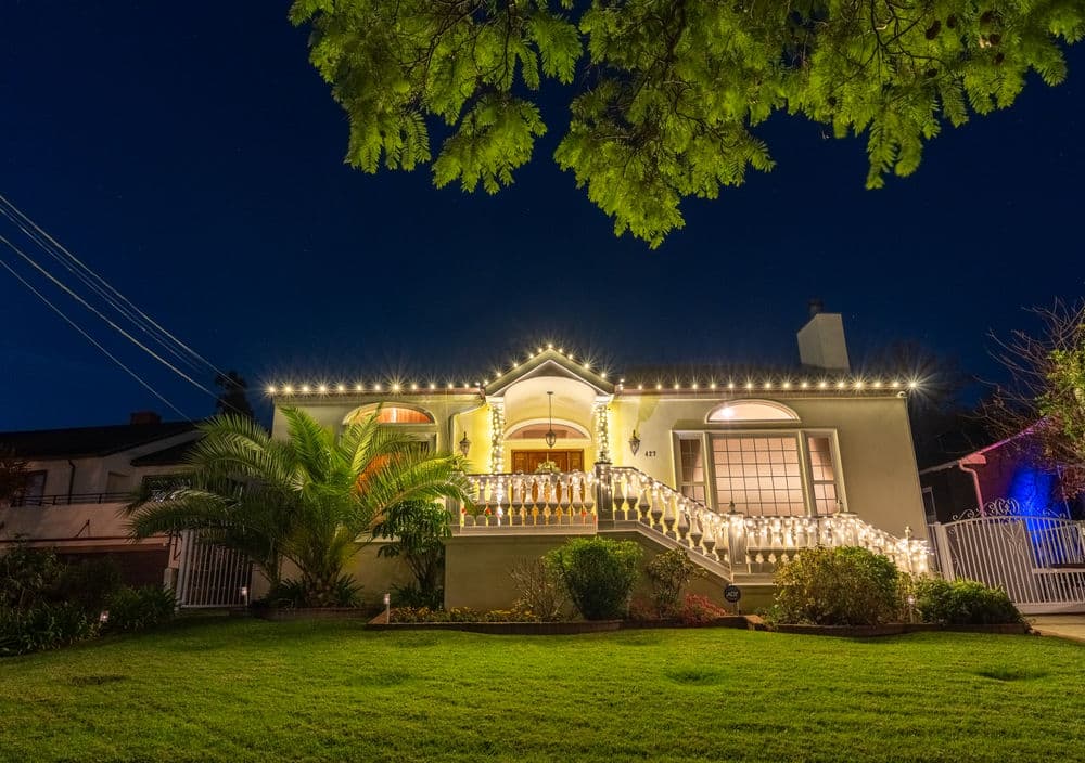 Charming illuminated house at night with decorative lights and well-maintained garden.