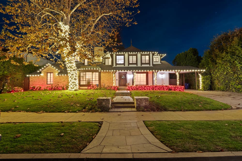 Charming house adorned with festive lights, surrounded by a well-maintained garden at night.